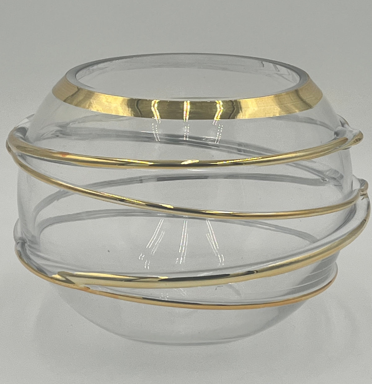 The Helixa Sphere 5.5x4.5 Op by Floral supplies Point is a round, clear glass vase with a wide opening and gold spiral metallic bands, embodying contemporary luxury against a plain light gray background.